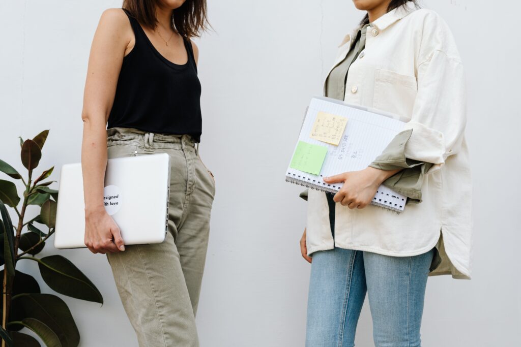 Image of 2 women talking with notepads -image by pexels-karolina-grabowska