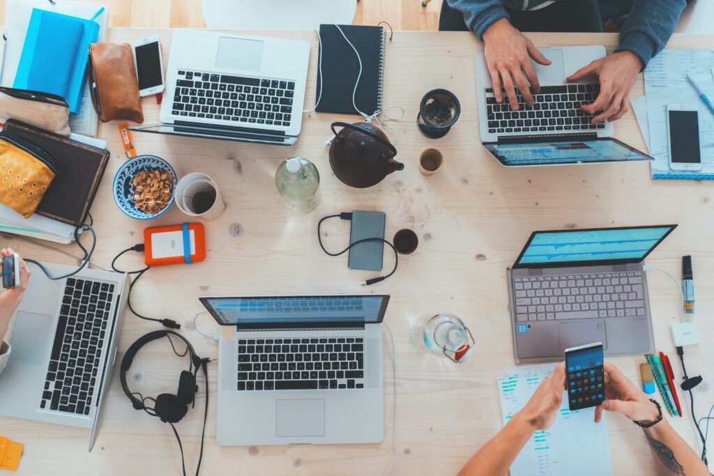 A birds eye point of view of a long desk with multiple people working, laptops and desk items as they are doing deep work
